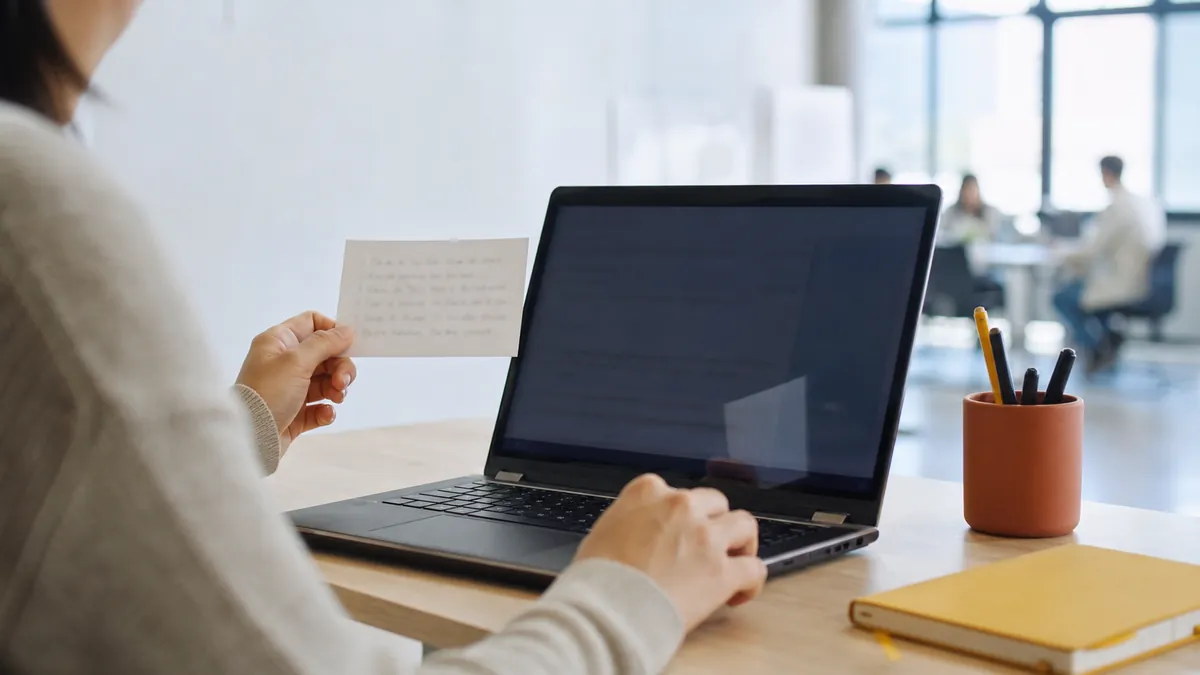 Hands reviewing a terminology card beside a laptop at a standing desk in a bright modern office